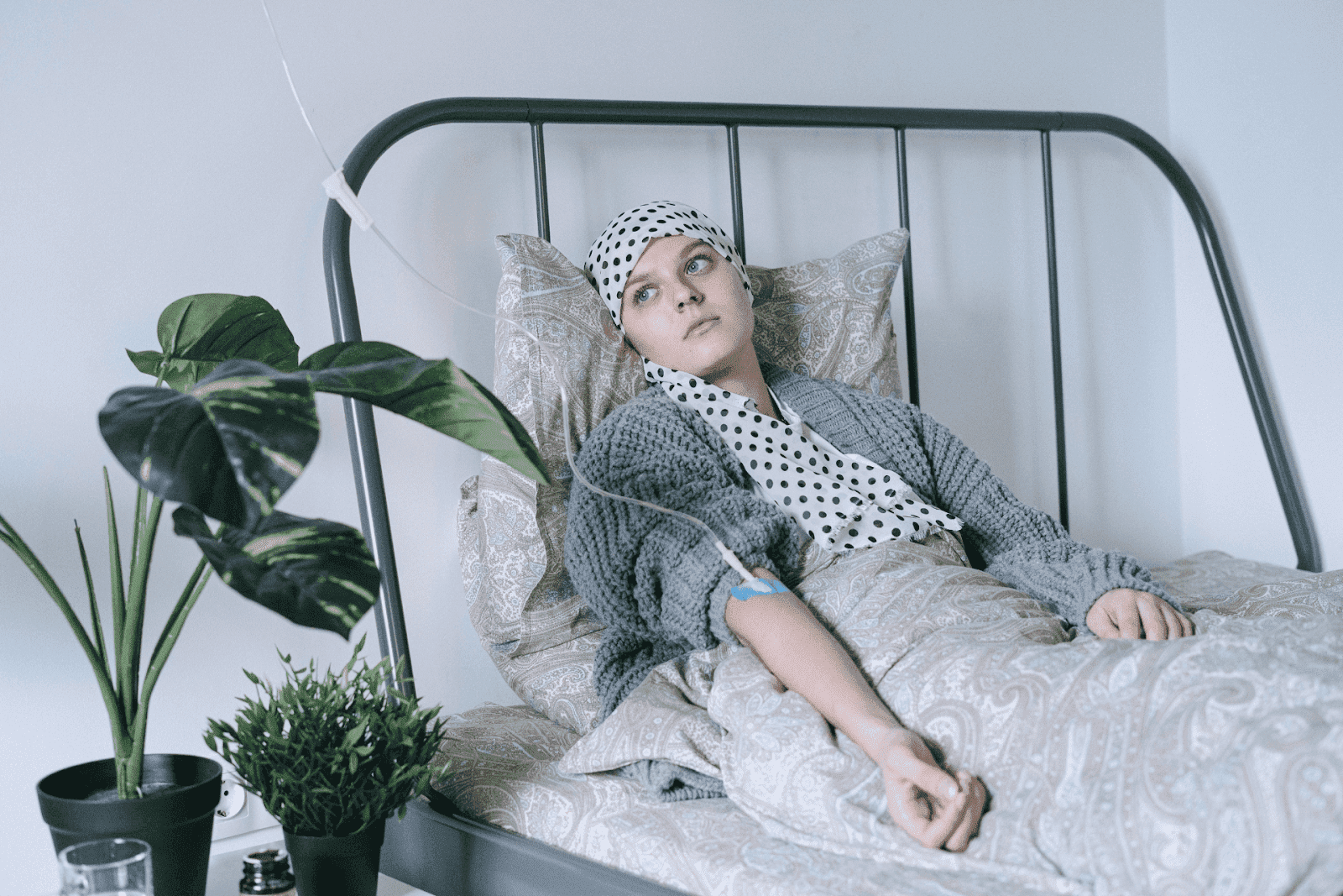 Person resting in bed with an IV line, wearing a headscarf and looking off to the side