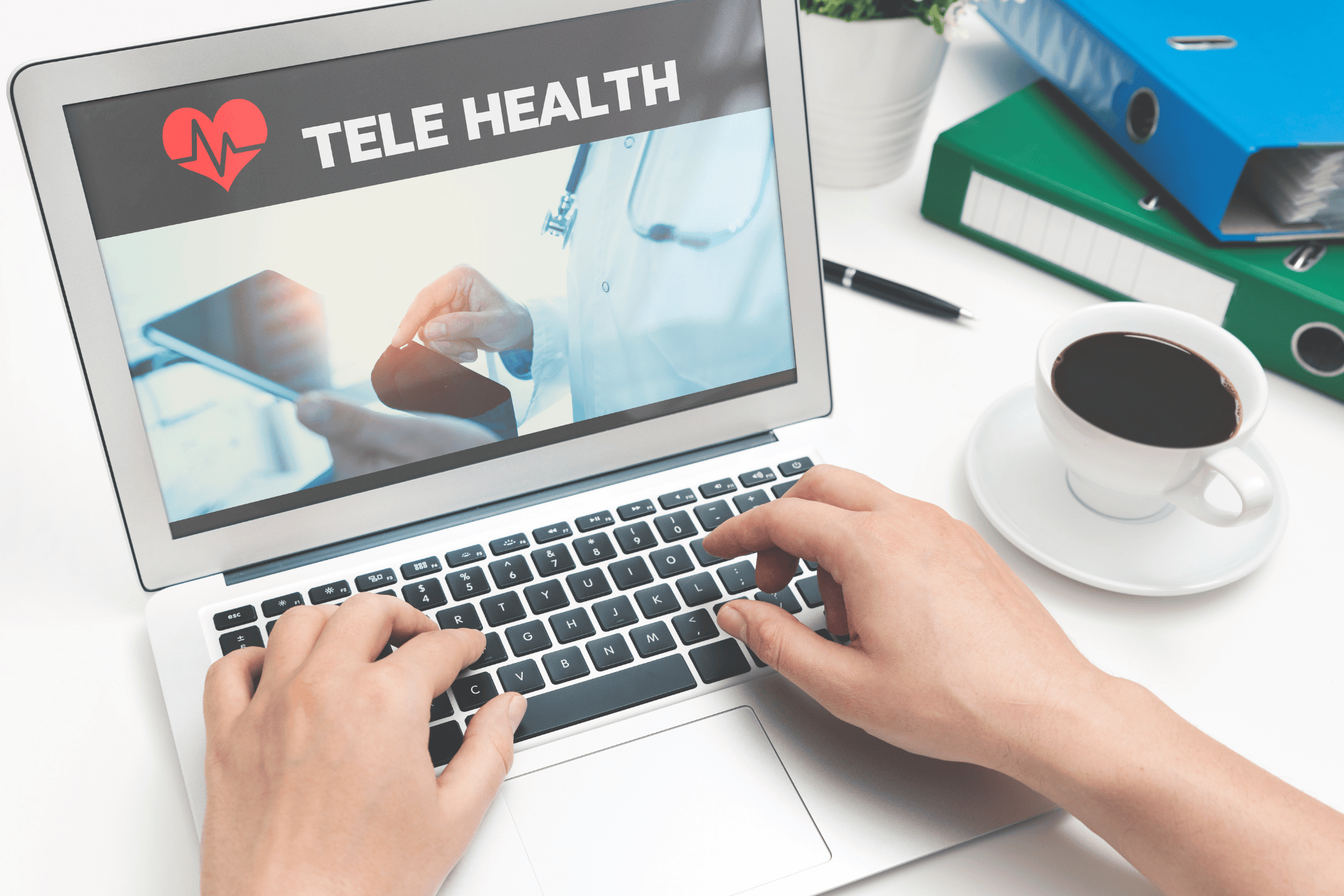 Person typing on a laptop showing a telehealth screen with a doctor and tablet image.