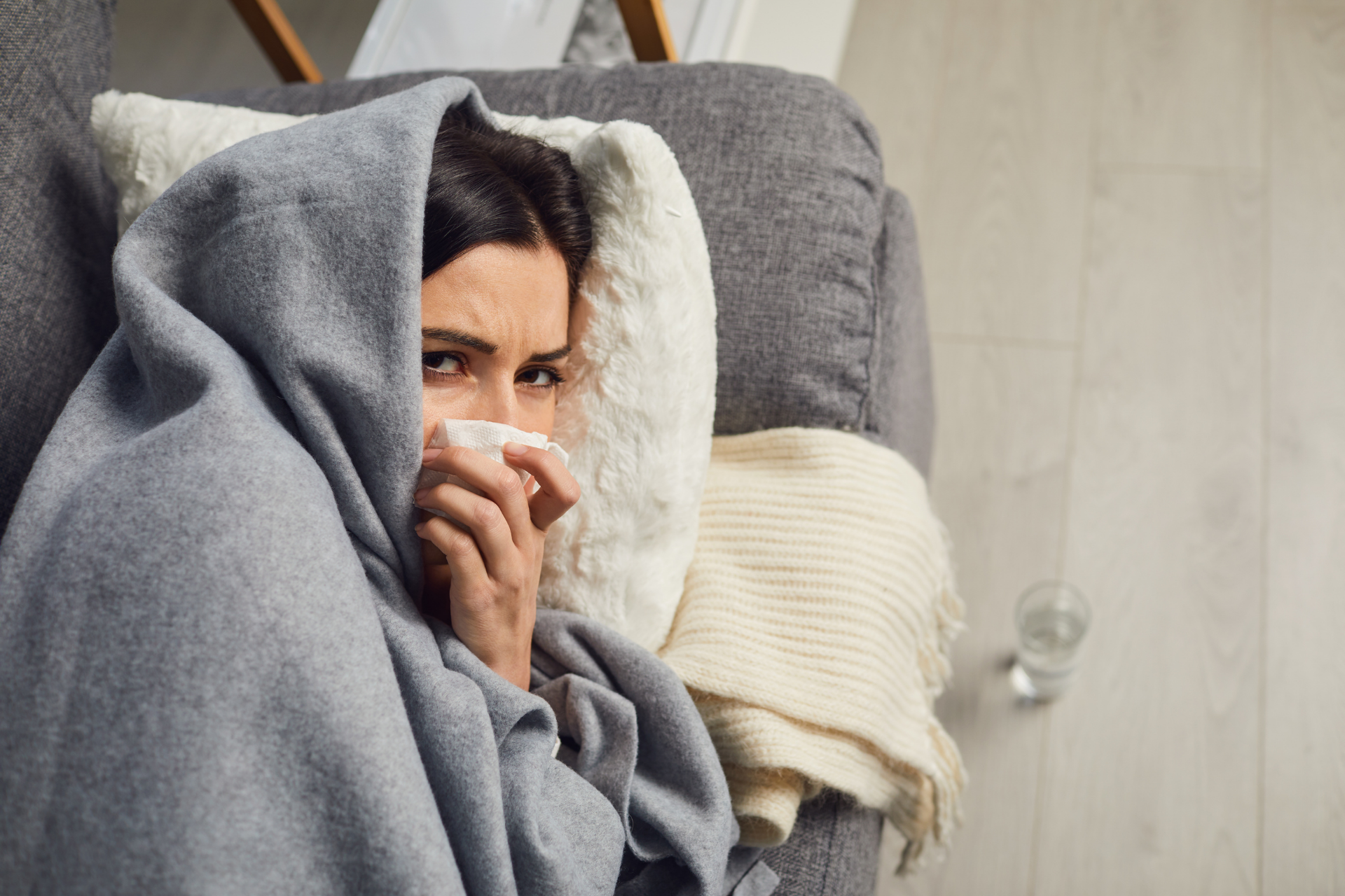 Person wrapped in a blanket holding a tissue while resting on a couch