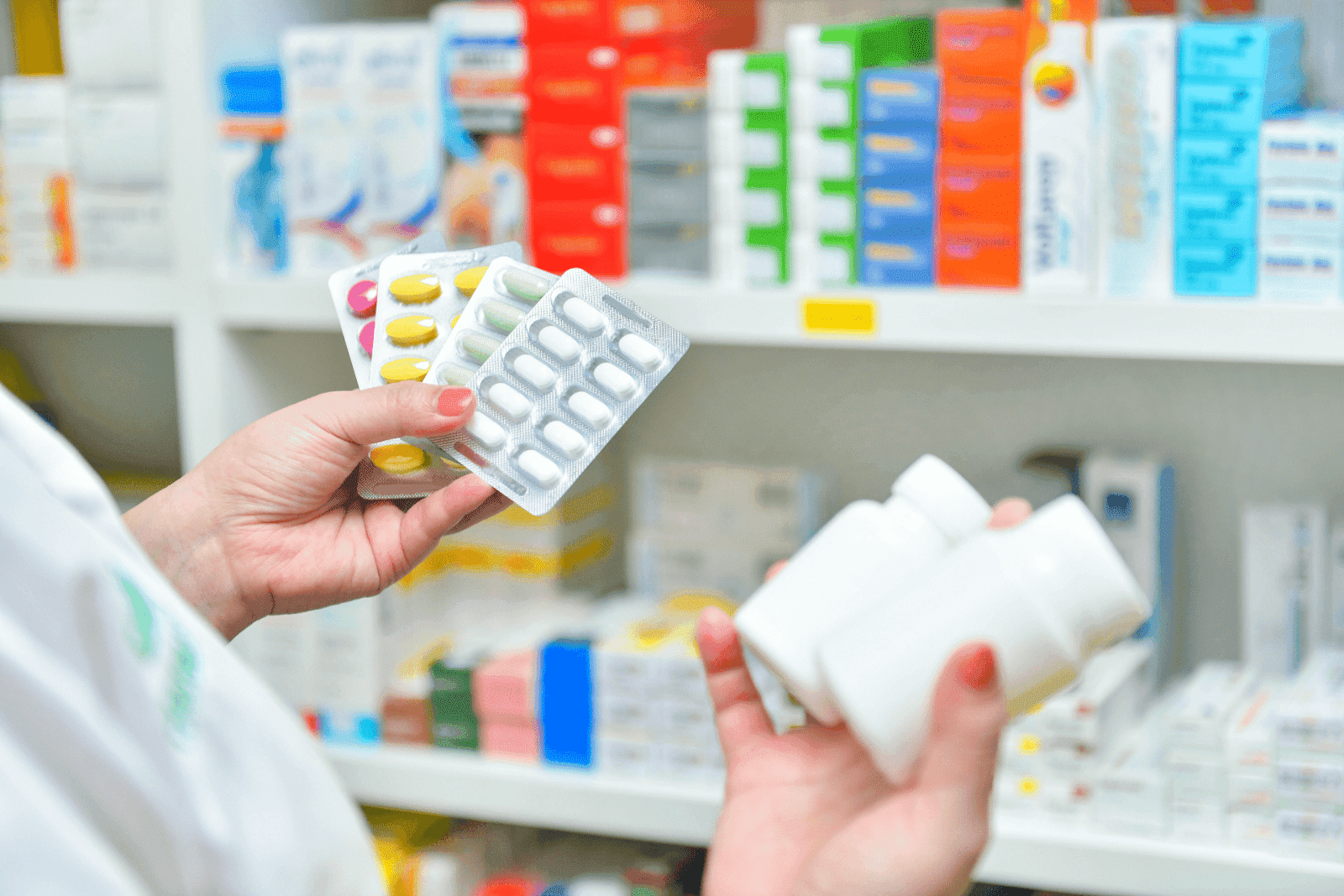 Pharmacist holding blister packs and pill bottles in front of shelves with medication