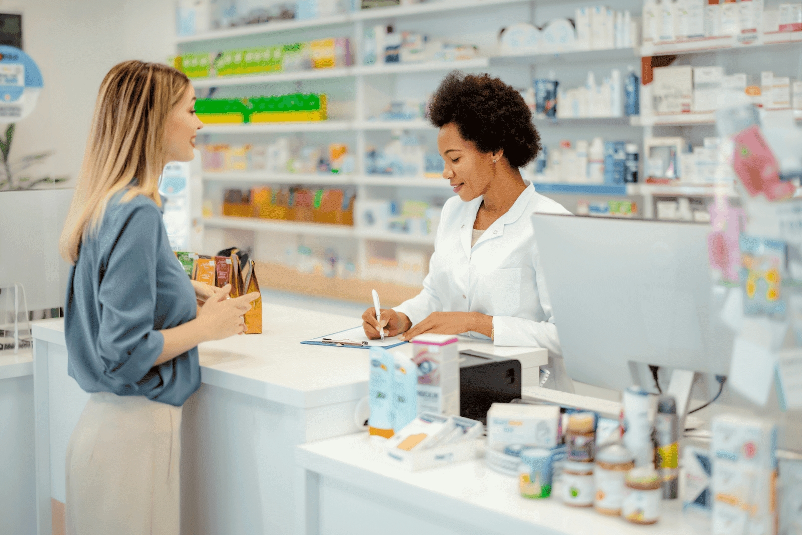 Pharmacist in a white coat assisting a customer at a pharmacy counter, with medicine shelves in the background.