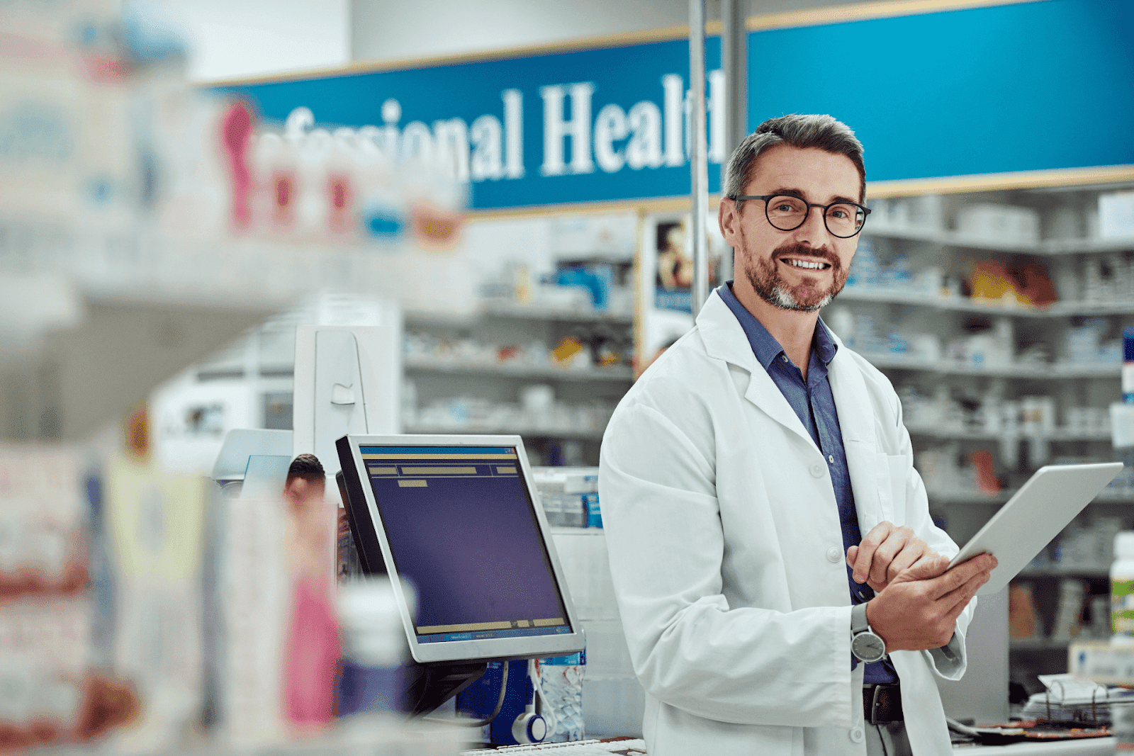 Pharmacist in a white coat holding a tablet and smiling in a pharmacy