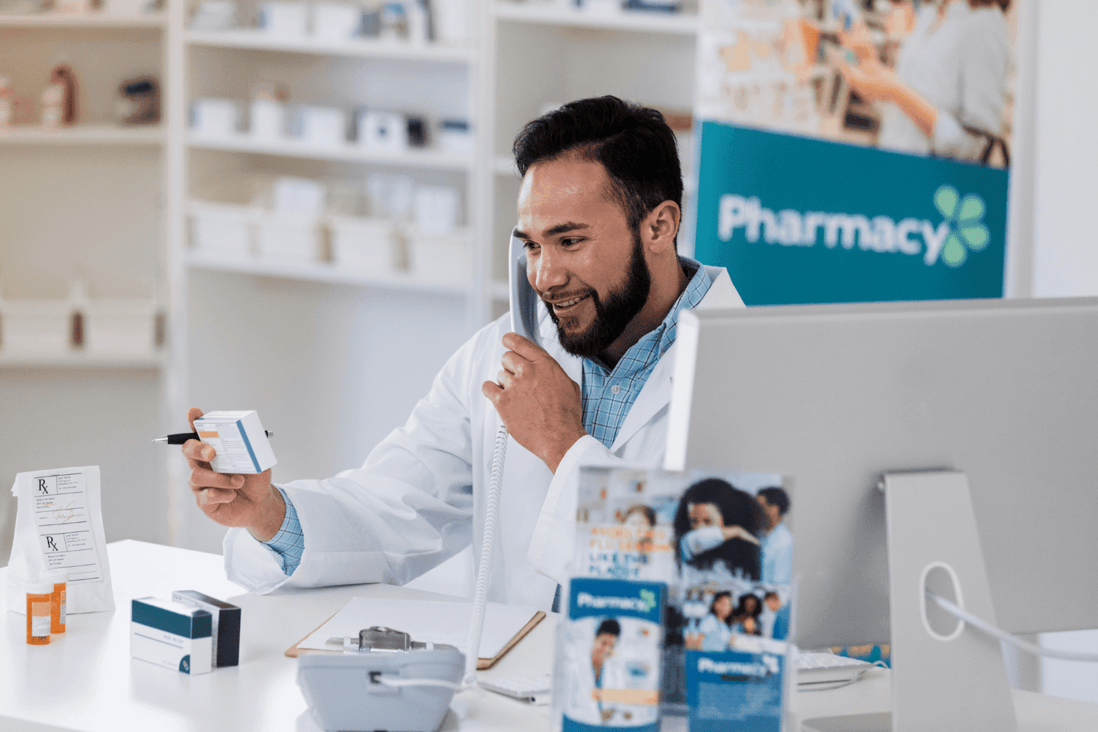 Pharmacist in a white coat talking on the phone while holding a medication box at the counter