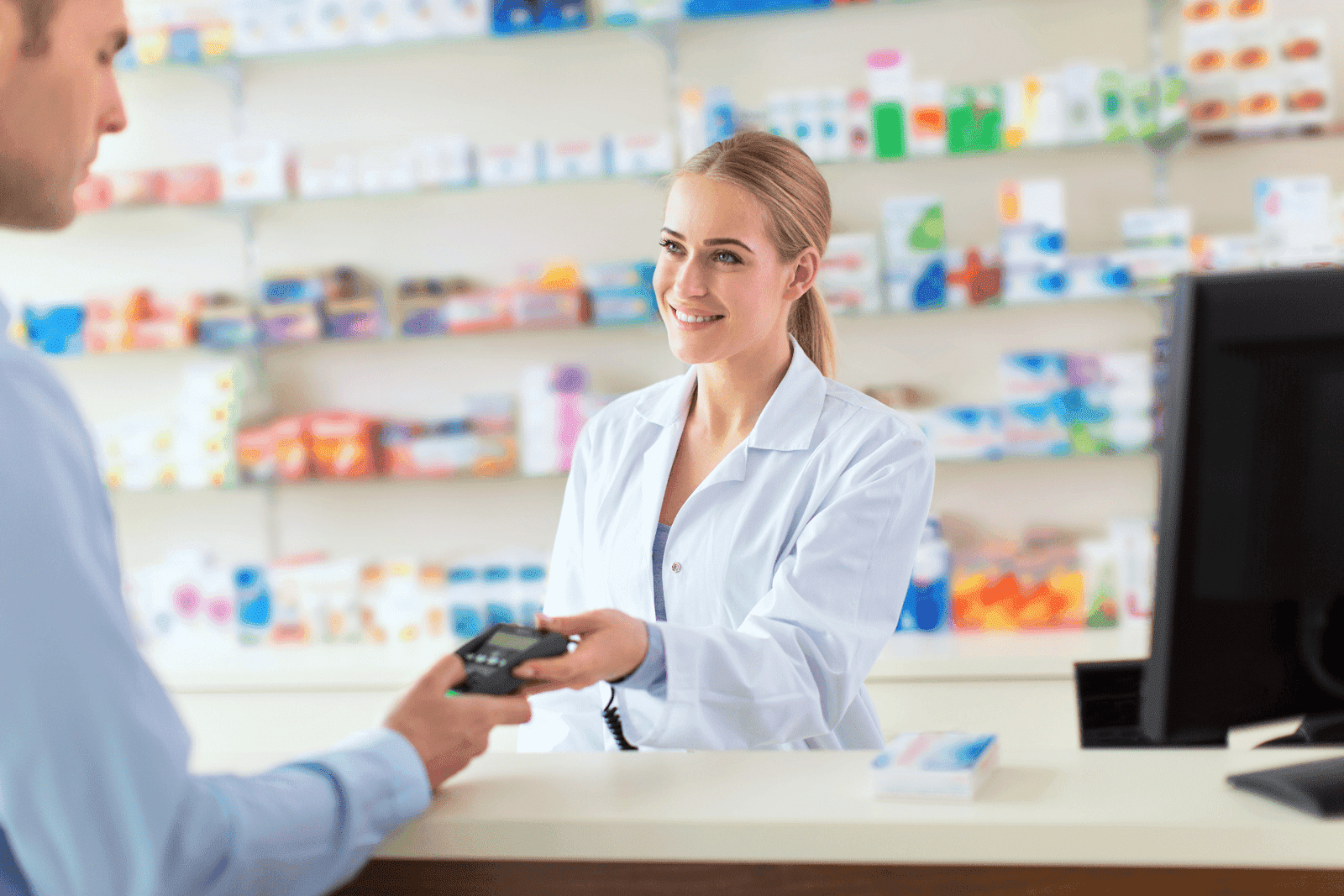 Pharmacist smiling while handing a payment terminal to a customer