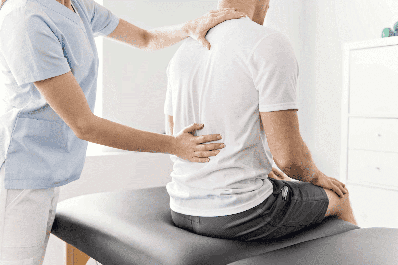 Physiotherapist examining a man’s back while he sits on a treatment table