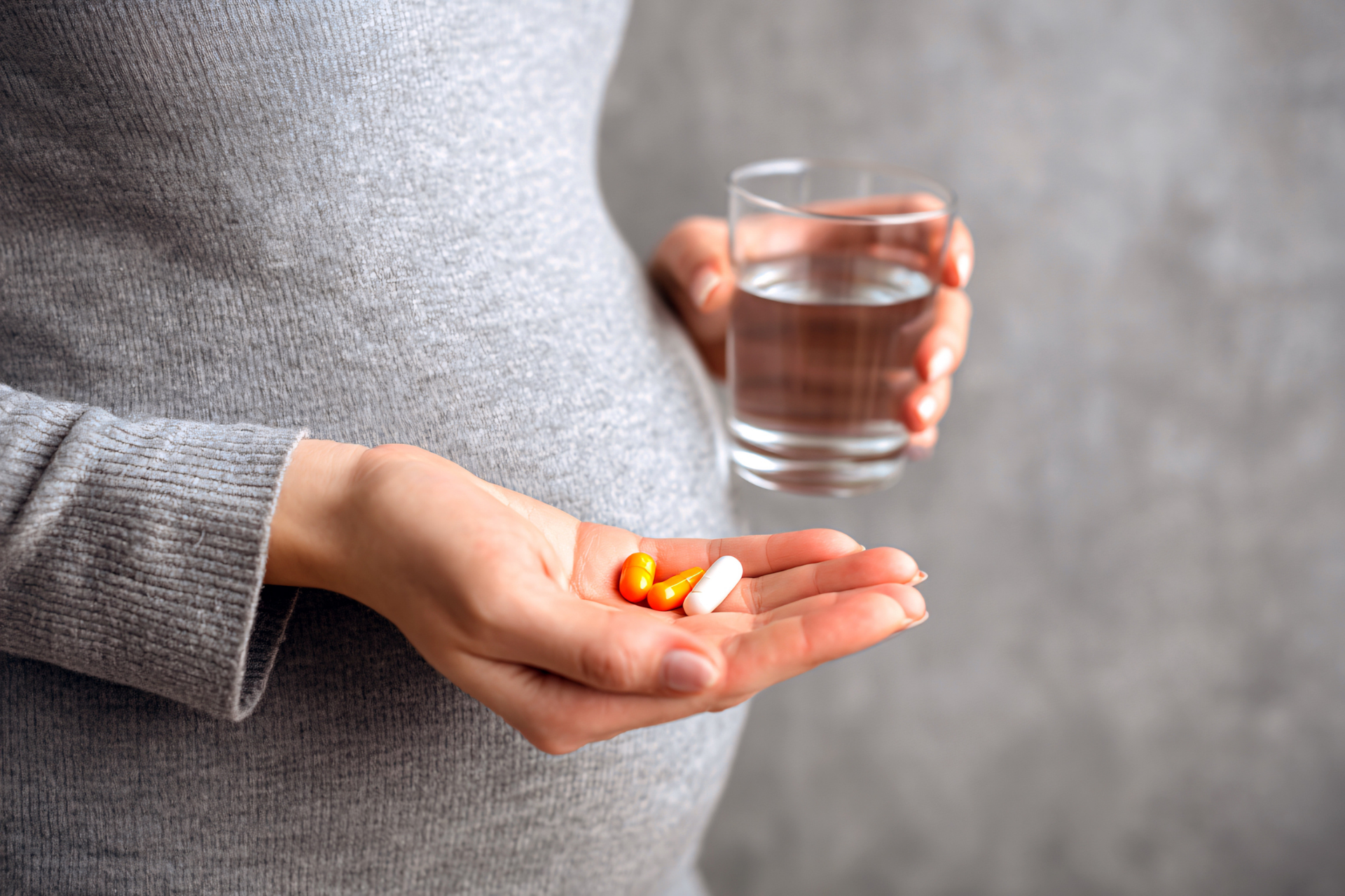 Pregnant woman holding pills in one hand and a glass of water in the other