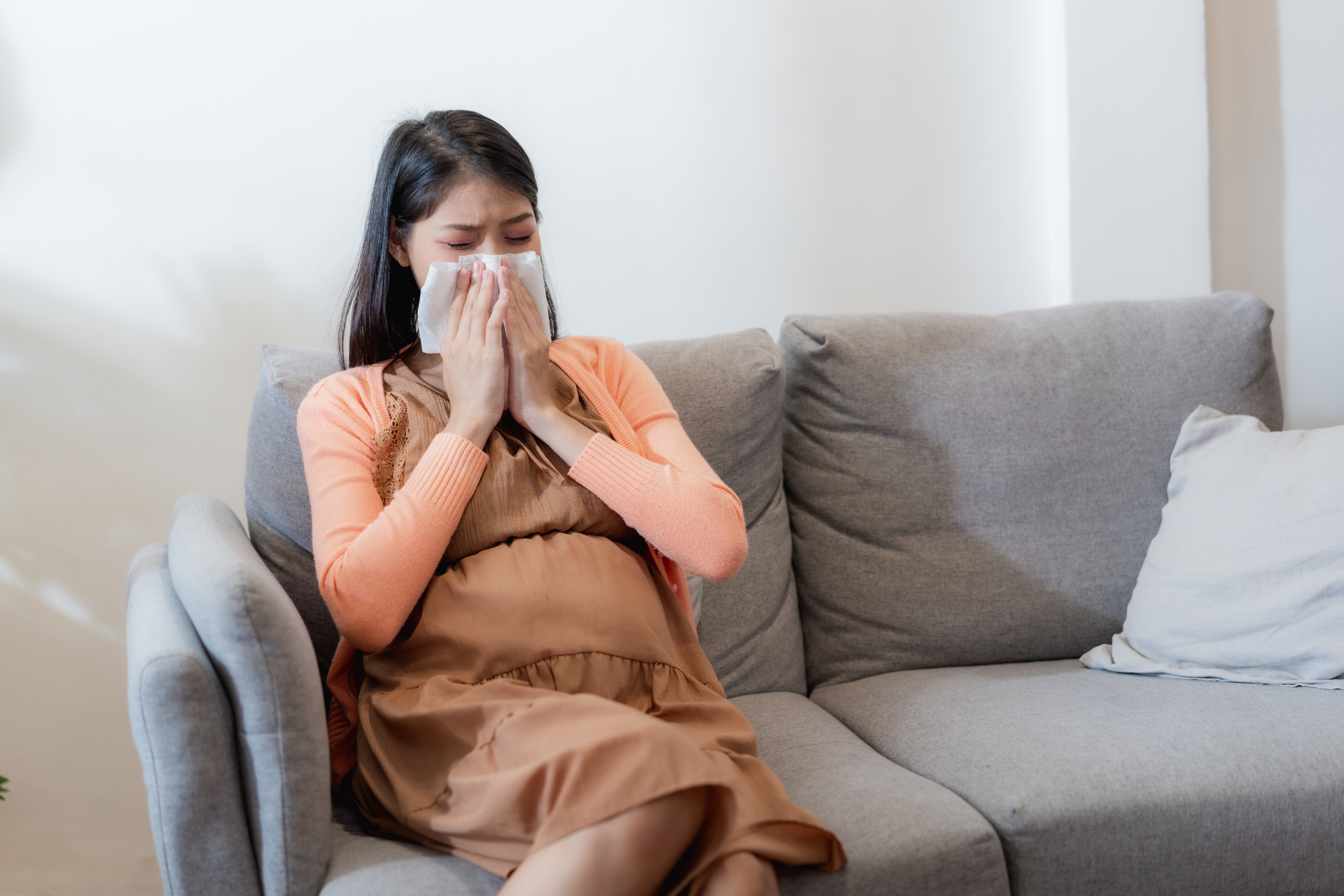 Pregnant woman sitting on a couch holding a tissue to her nose
