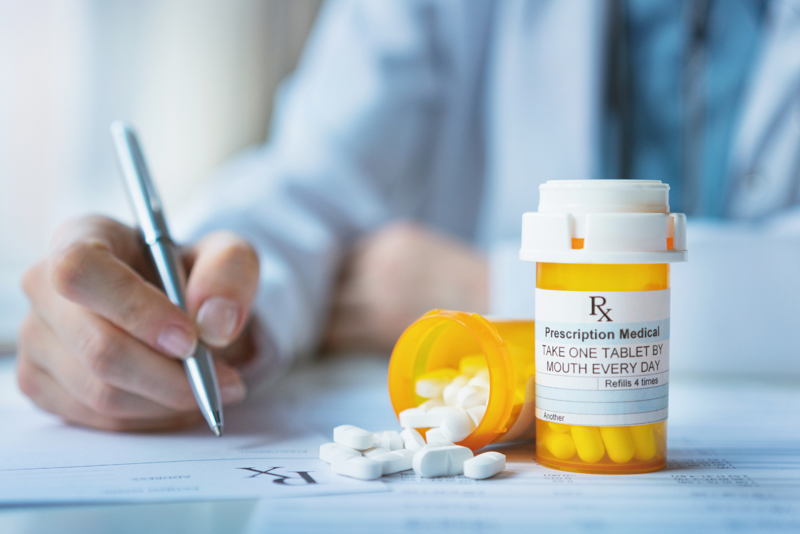 Prescription pill bottle with tablets spilling out, next to a doctor writing on a prescription form