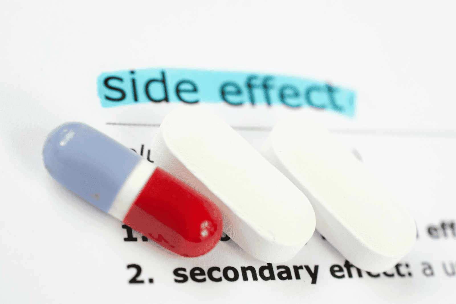 Red, blue, and white capsule pills placed on a document labeled ‘side effects.