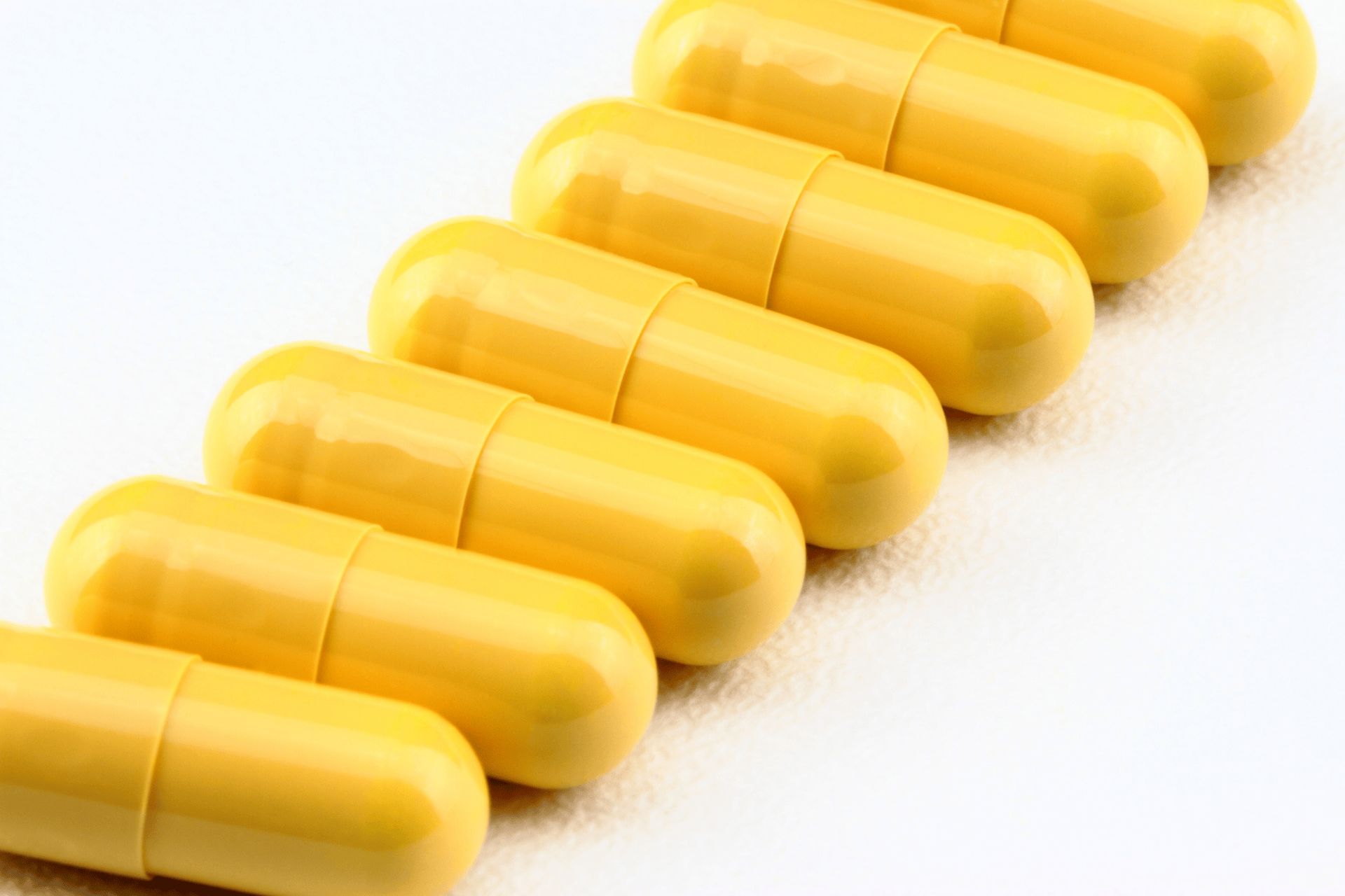 Row of yellow capsules arranged neatly on a white surface.