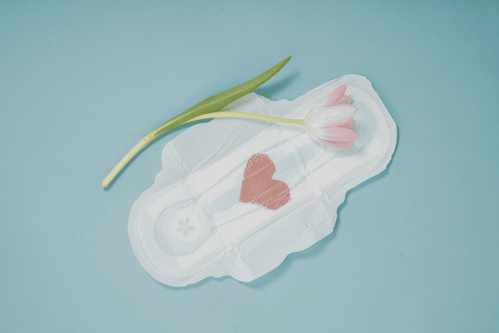 Sanitary pad with a red heart-shaped stain and a pink tulip on a blue background.