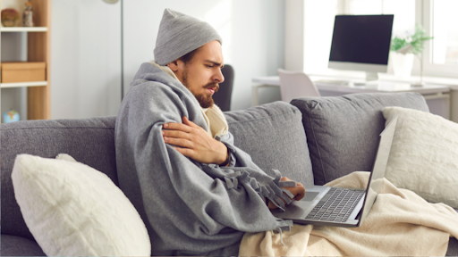 Man sitting on couch with a blanket shivering due to a high fever
