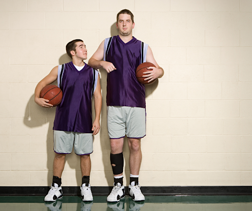 Two men holding basketballs, one is significantly taller than the other.