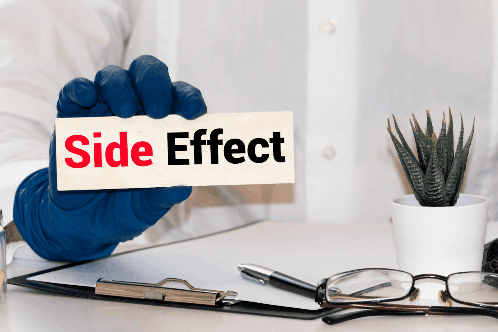 Gloved hand holding a sign reading ‘Side Effect’ on a medical desk.
