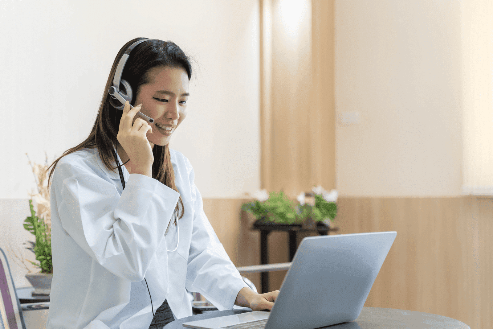 Smiling doctor wearing a headset while talking to a patient on a laptop.