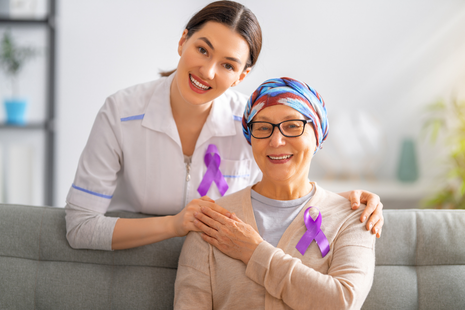 Smiling nurse and cancer patient wearing purple awareness ribbons.