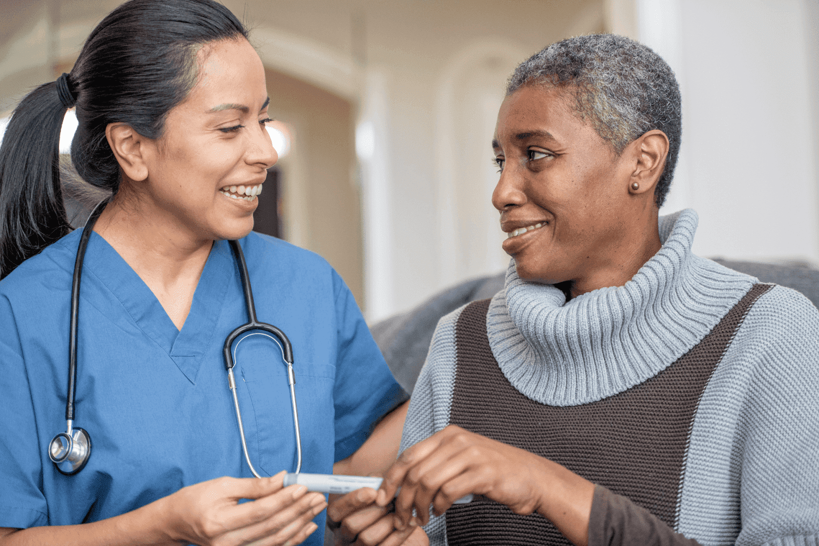 Smiling nurse talking with an older woman while holding a glucose testing device.