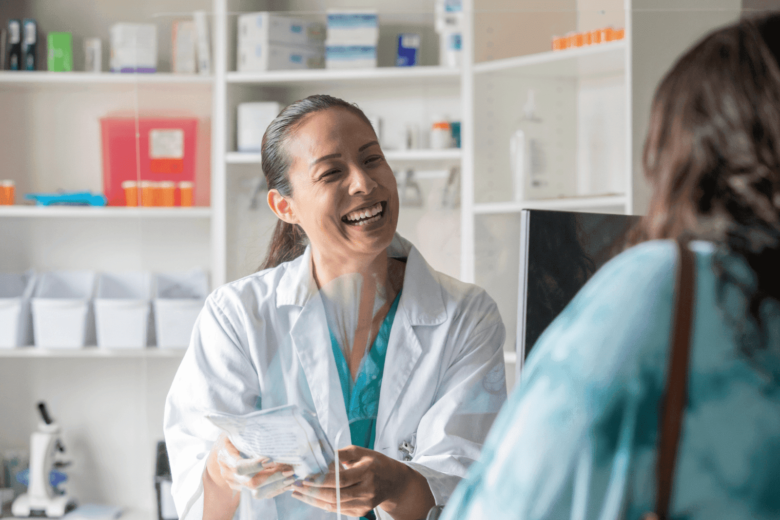 Smiling pharmacist handing prescription medicine to a customer.