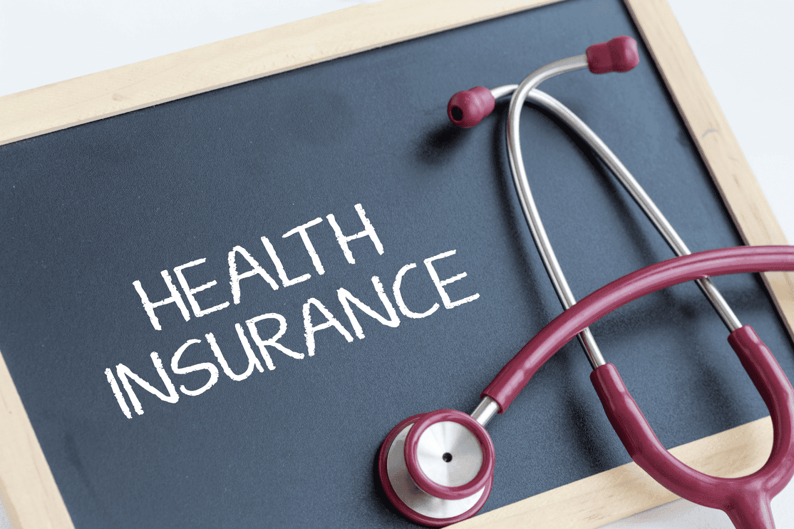 Stethoscope resting on a chalkboard with the words ‘Health Insurance’ written on it