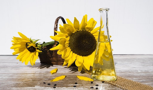 Sunflowers in a rustic basket with a sleek glass oil container nearby.