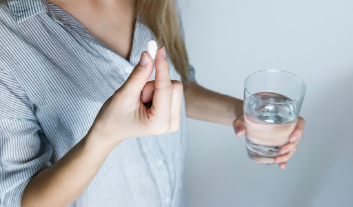 Close-up of a woman's hands holding a pill and a glass of water.