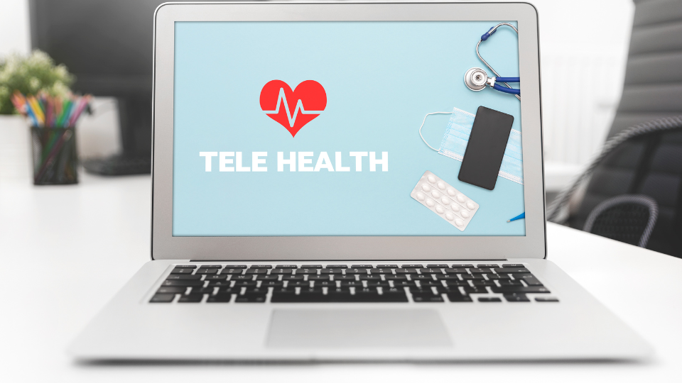 Laptop with “Telehealth” on desktop and medical items like a mask, pills, and a stethoscope