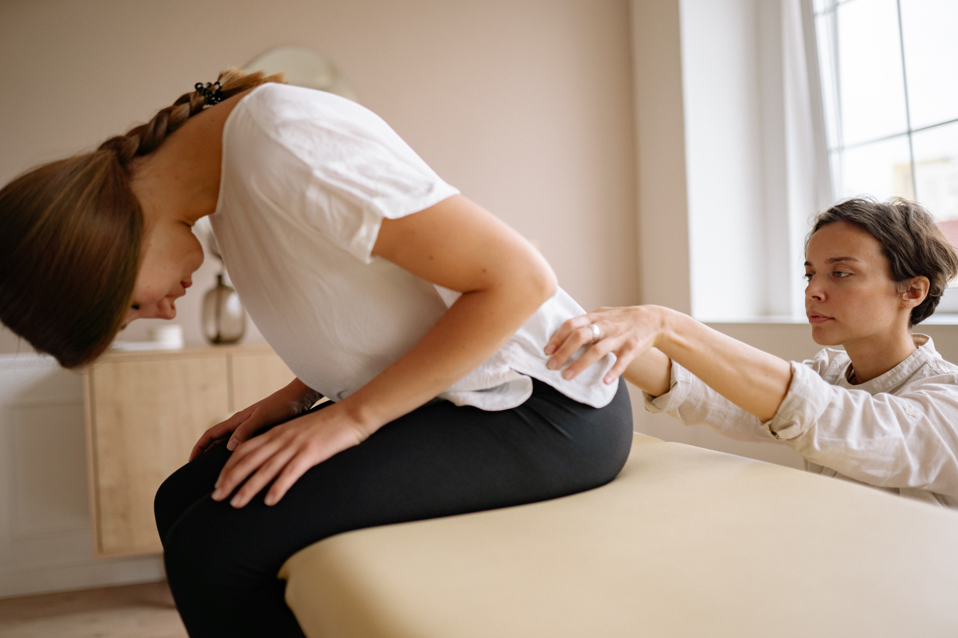 Therapist assessing a woman’s spine posture while she bends forward during an exam