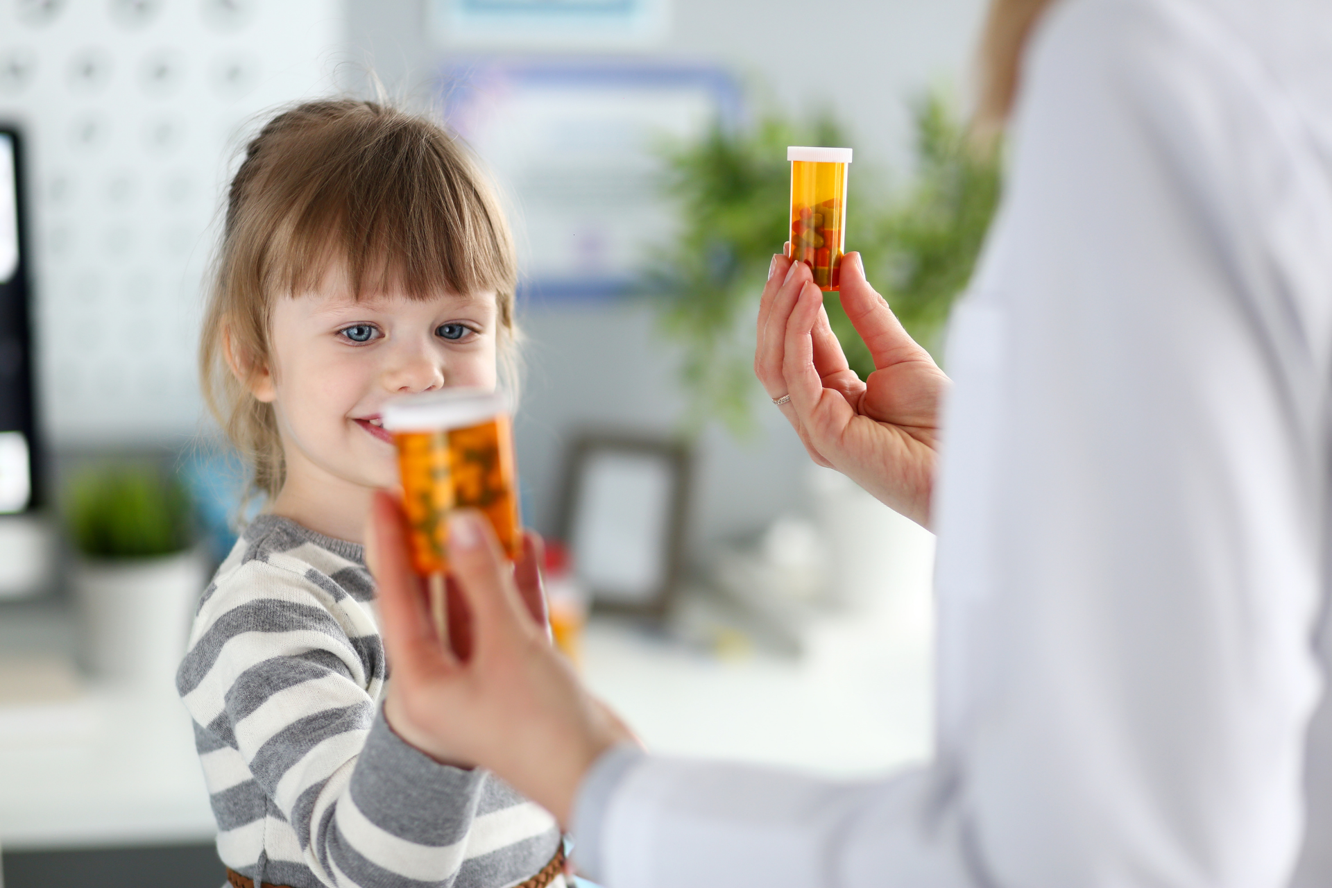 Toddler smiling while a healthcare provider holds up prescription pill bottles during a medical visit