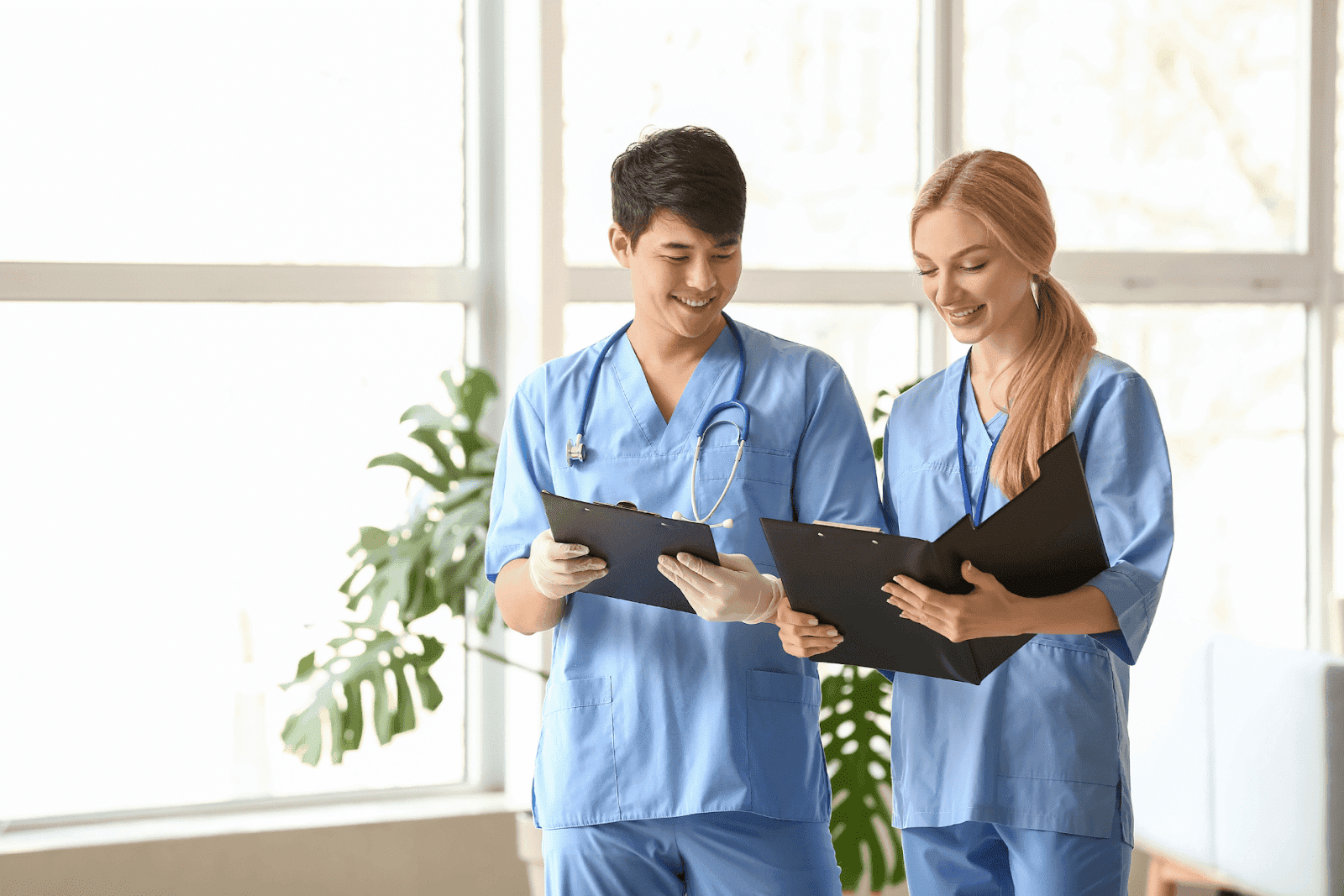 Two healthcare professionals in blue scrubs reviewing patient charts together.