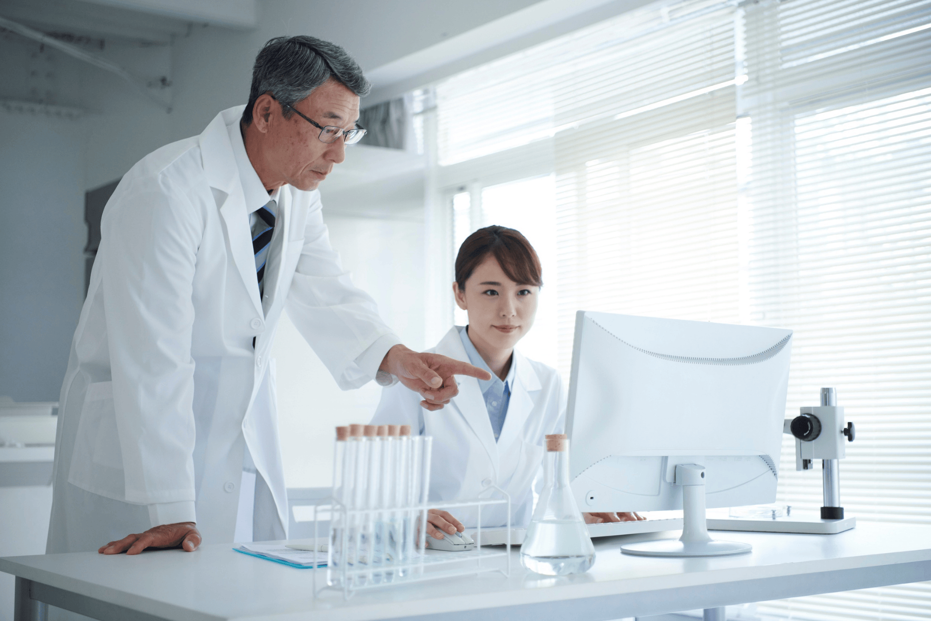Two scientists in lab coats working together at a computer in a bright laboratory.