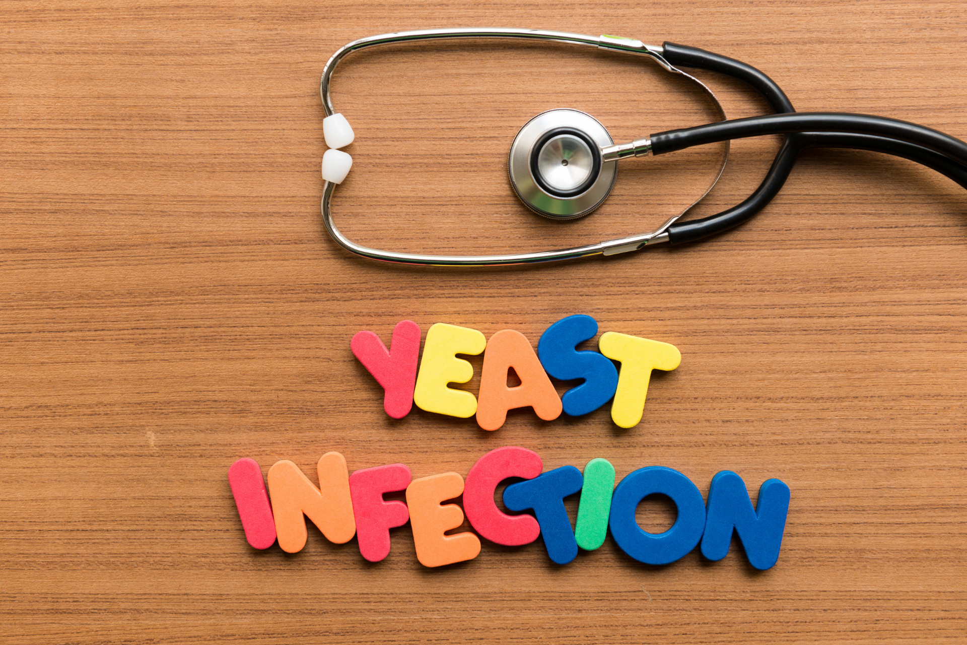 Stethoscope on a wooden surface above colorful letters spelling ‘Yeast Infection.