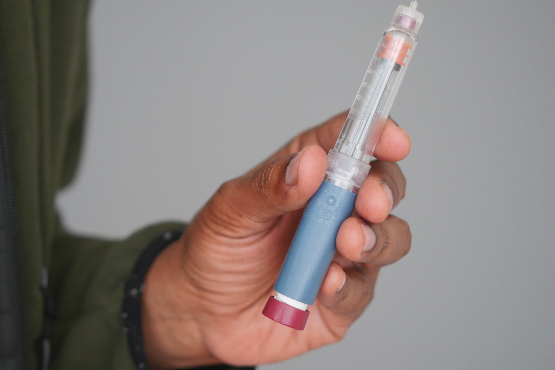 Hand holding a medication injection pen with a clear syringe chamber and blue body