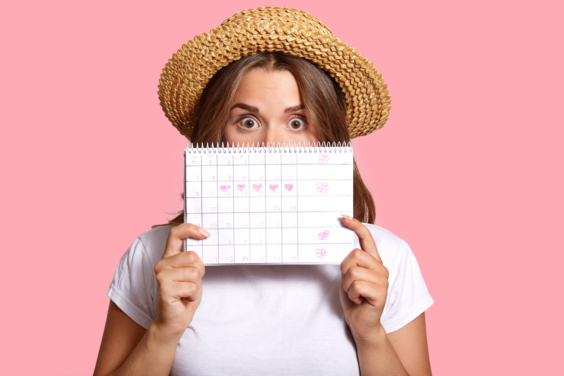 Woman holding a menstrual cycle calendar in front of her face against a pink background