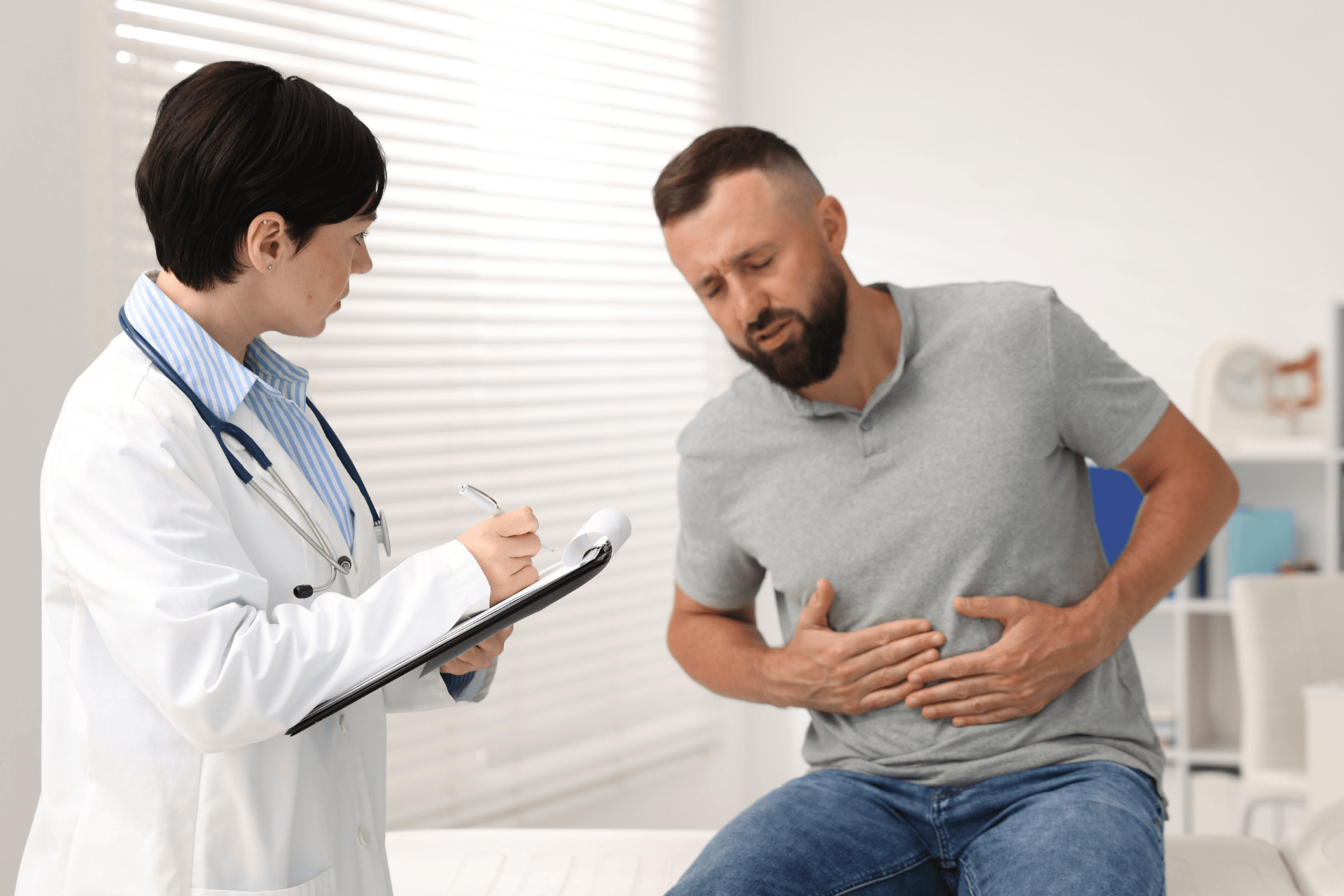 Doctor taking notes while examining a man with stomach pain.