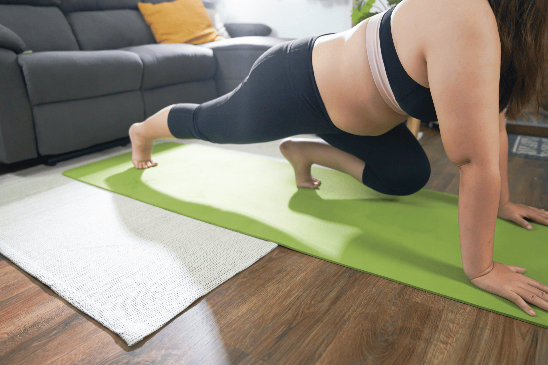 Person exercising on a green yoga mat in a living room.
