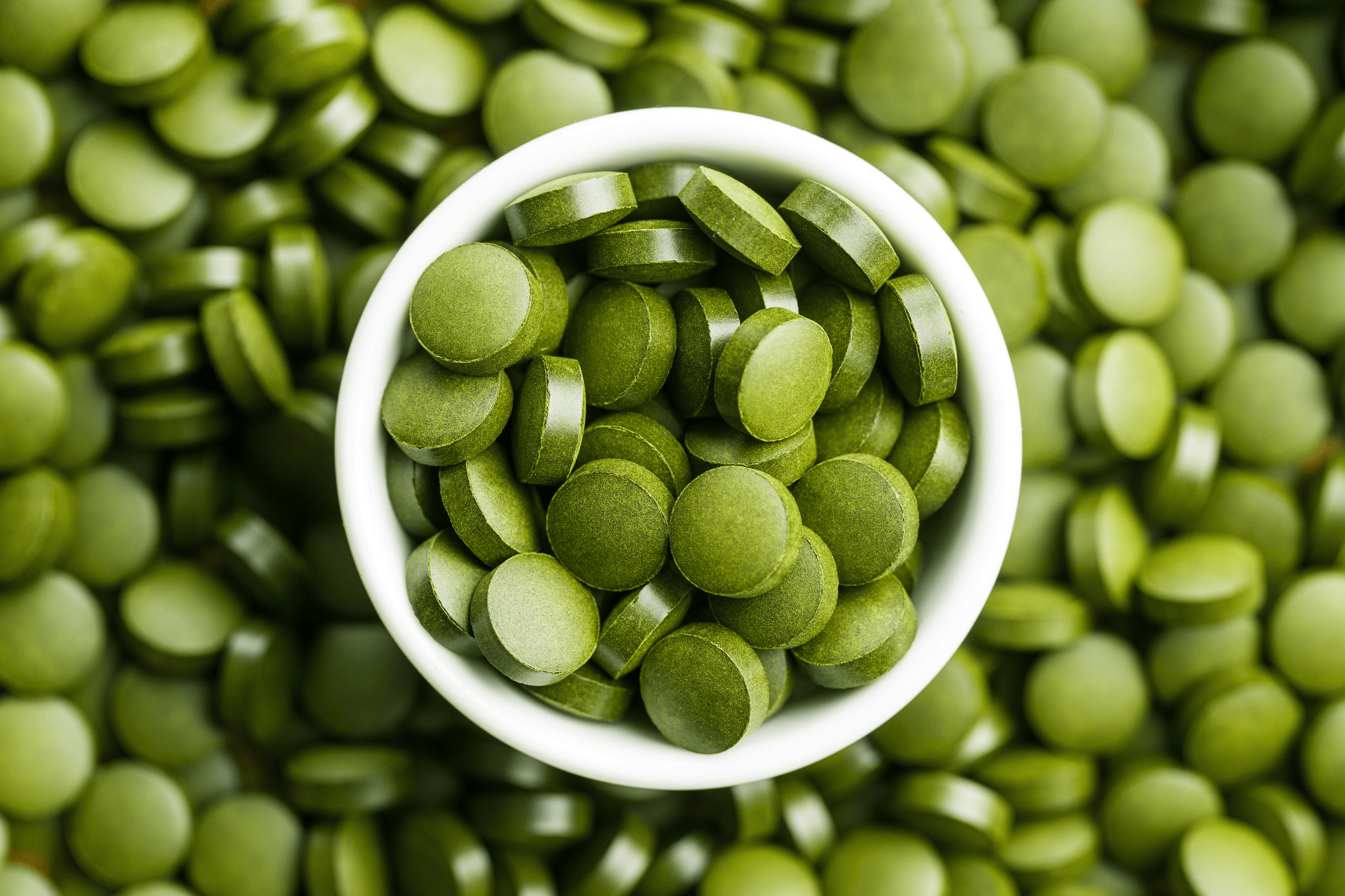 Close-up of green tablets in and around a white bowl.