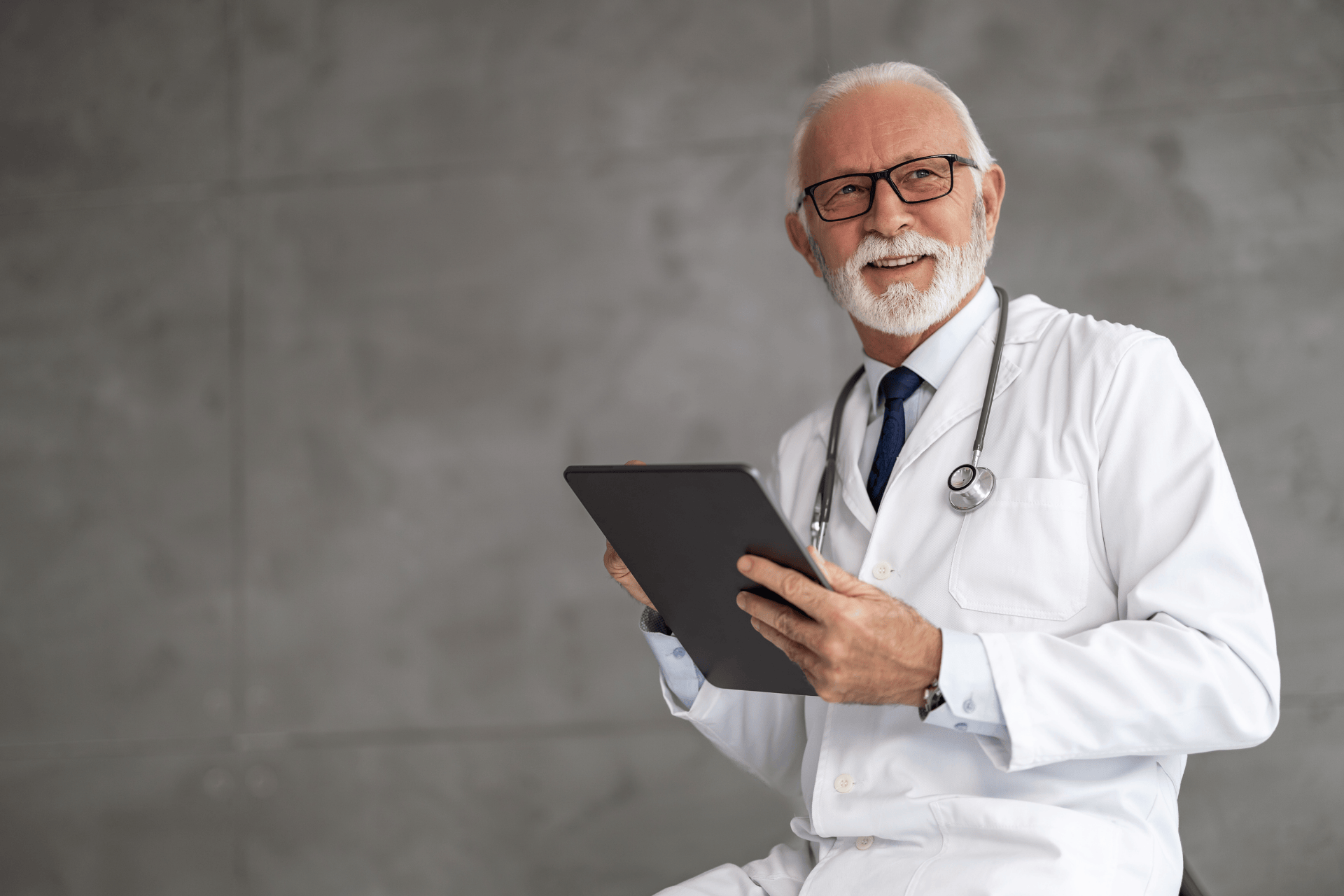 Smiling doctor in a white coat holding a tablet.