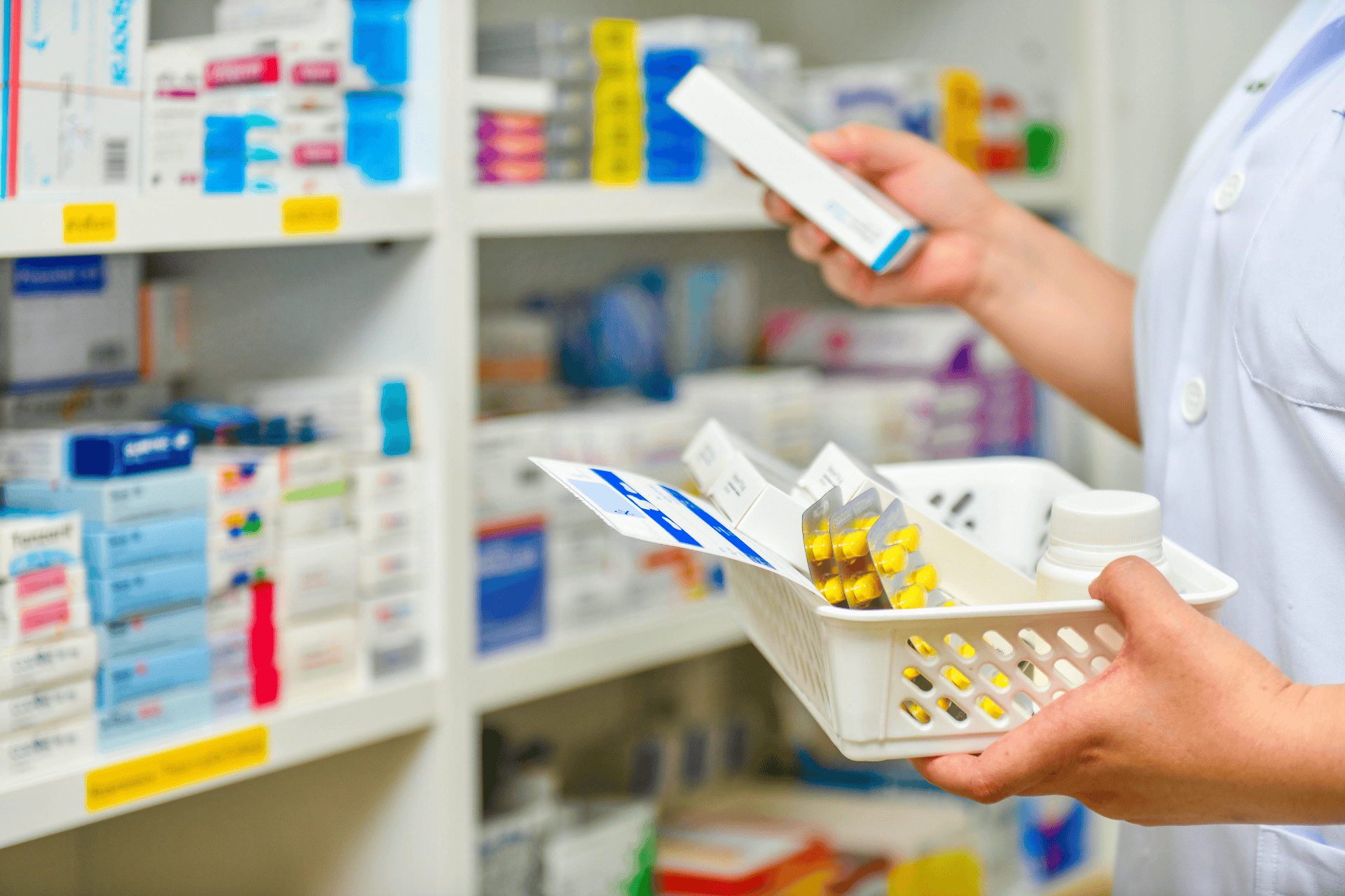 Pharmacist holding a basket of medicines while selecting a product from a pharmacy shelf.