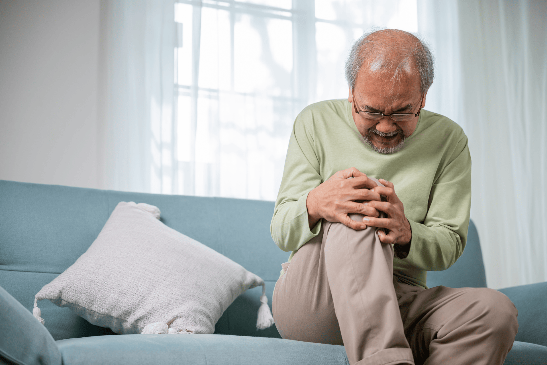 Older man sitting on a couch holding his knee in pain.