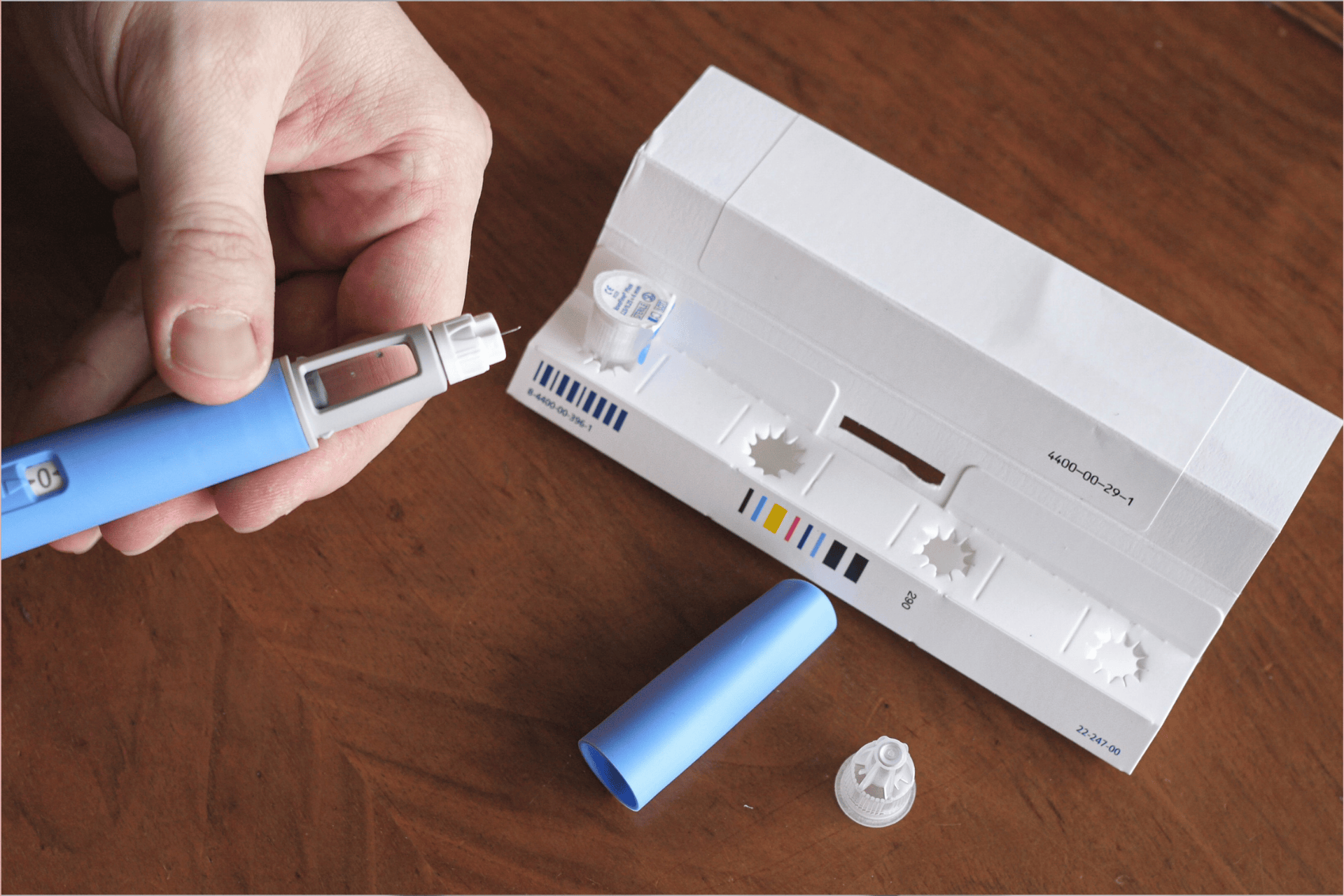 Person preparing an insulin pen with packaging and cap on a table.