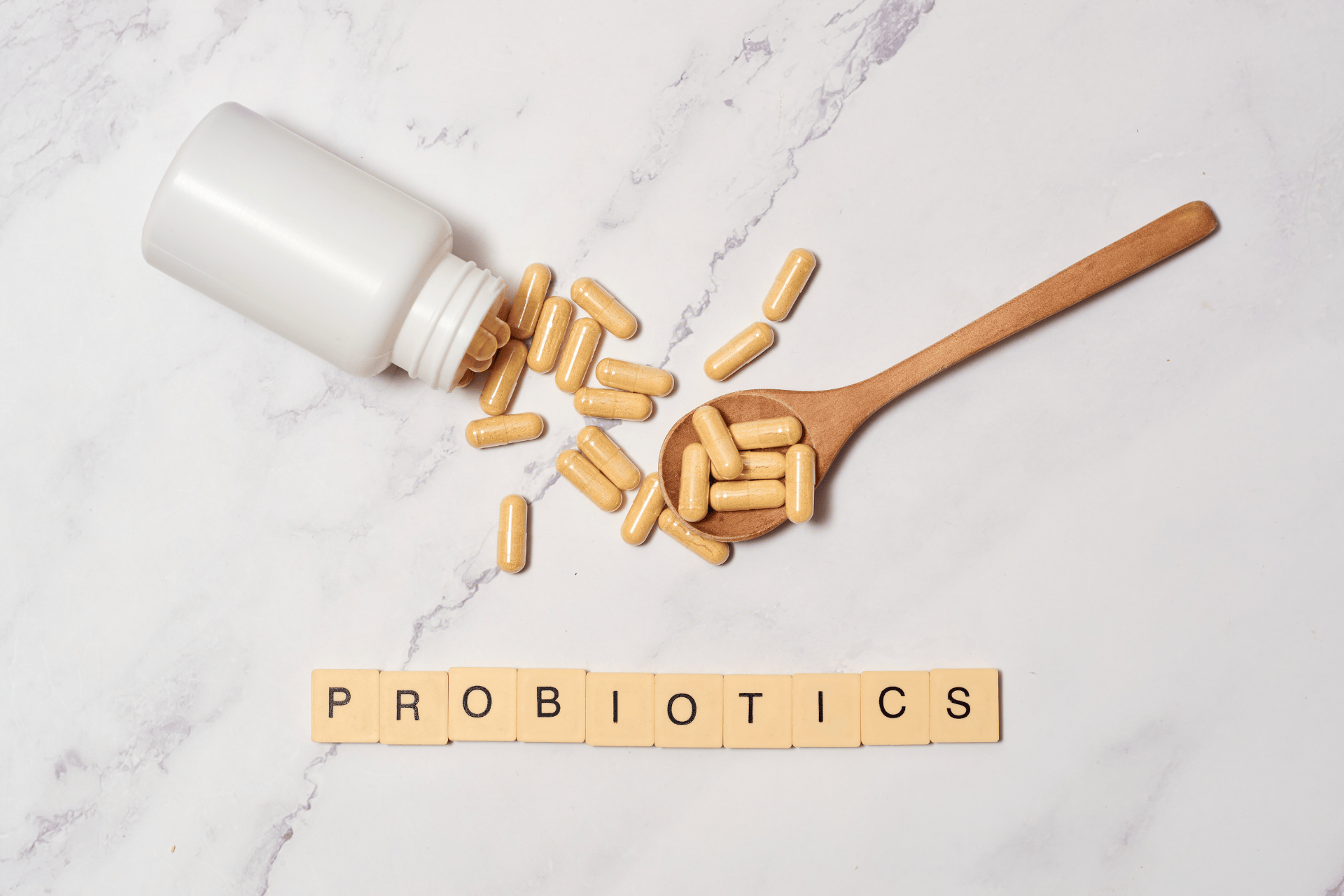Probiotic capsules spilled from a bottle with a wooden spoon and the word probiotics spelled out.