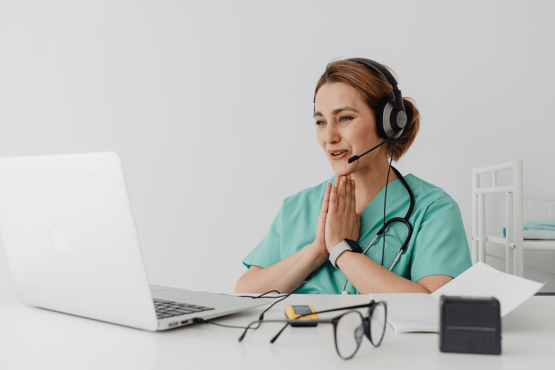 Female healthcare worker in scrubs using a laptop for an online consultation.