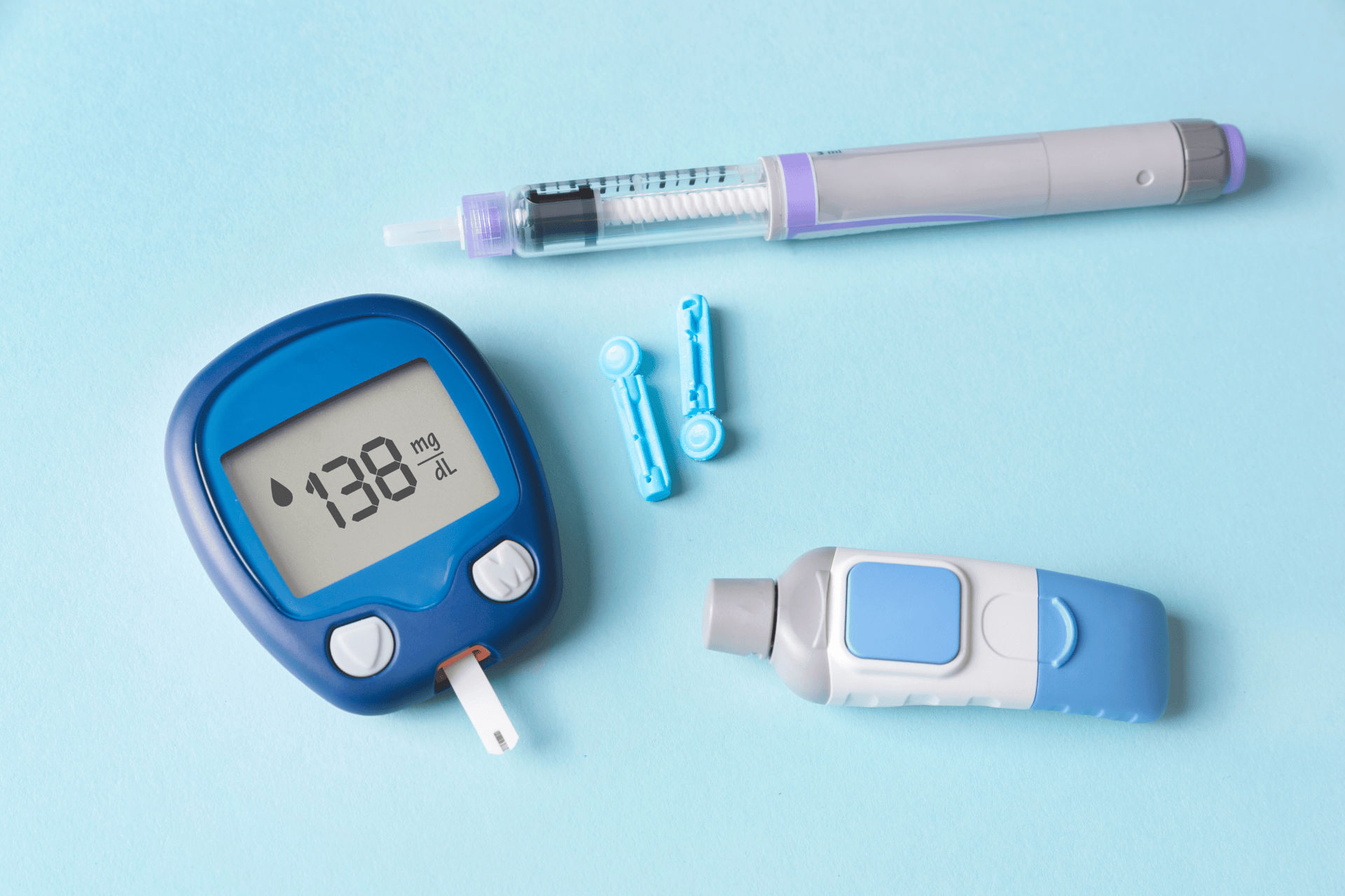 Diabetes monitoring kit with glucometer, insulin pen, and lancets on a blue background.