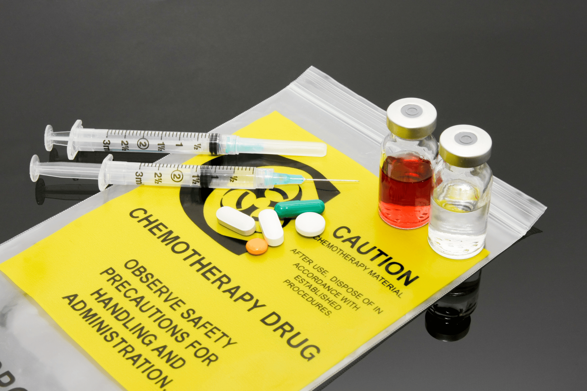 Chemotherapy drugs, syringes, and pills on a caution-labeled medical bag.
