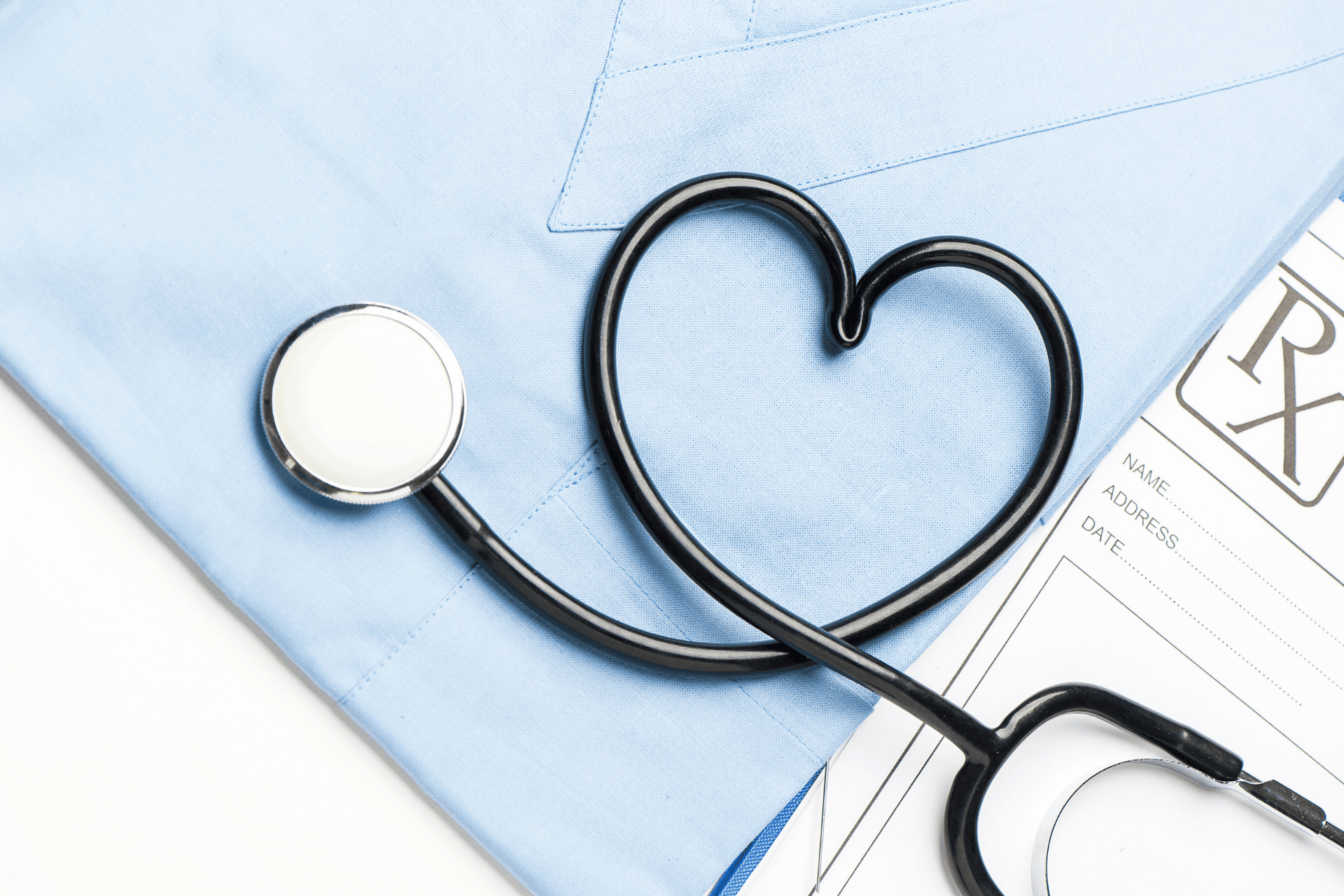Stethoscope shaped like a heart on medical scrubs beside a prescription pad.