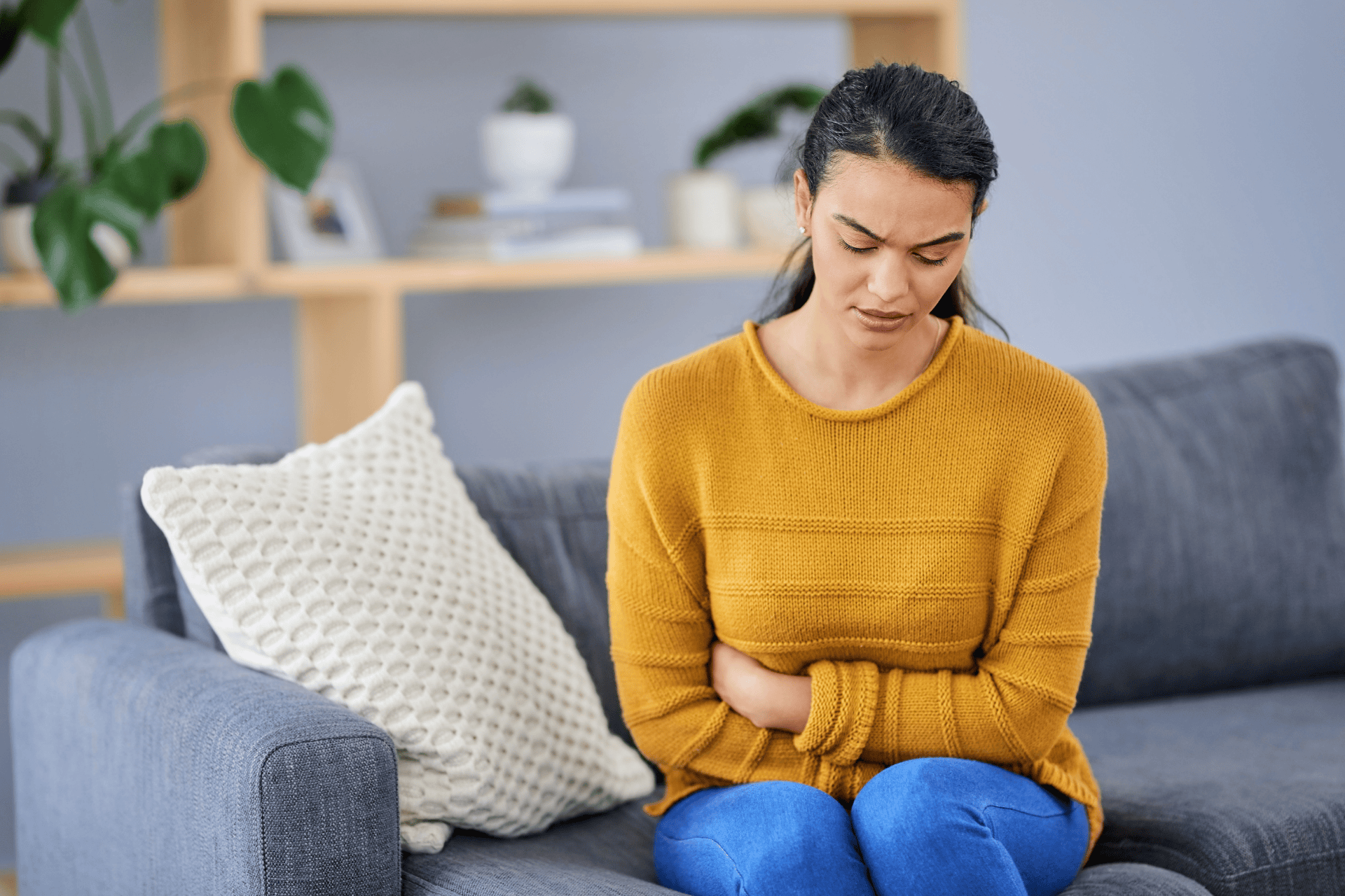 Woman sitting on a couch holding her stomach in discomfort.