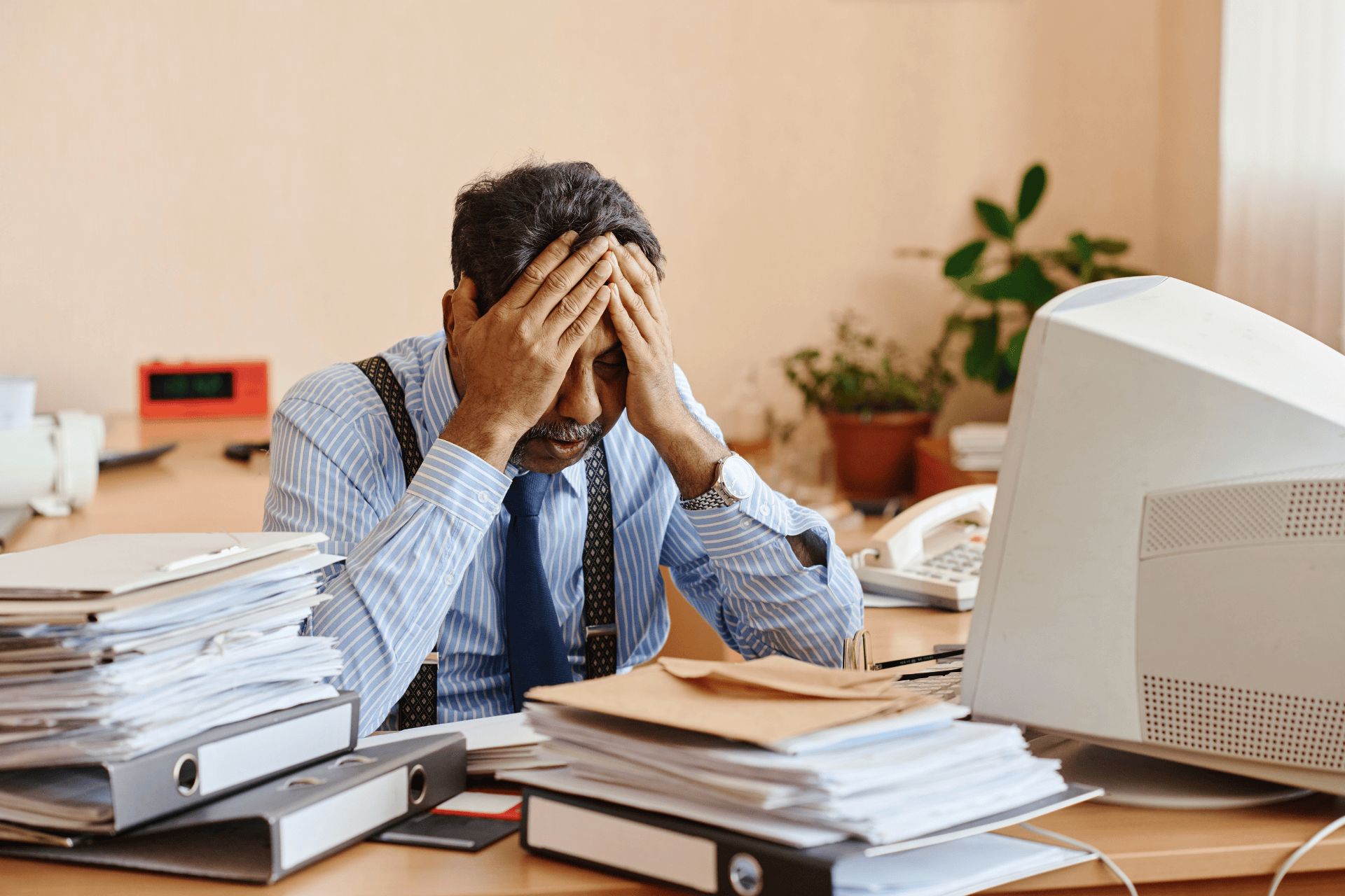 Stressed man sitting at a cluttered desk with his head in his hands