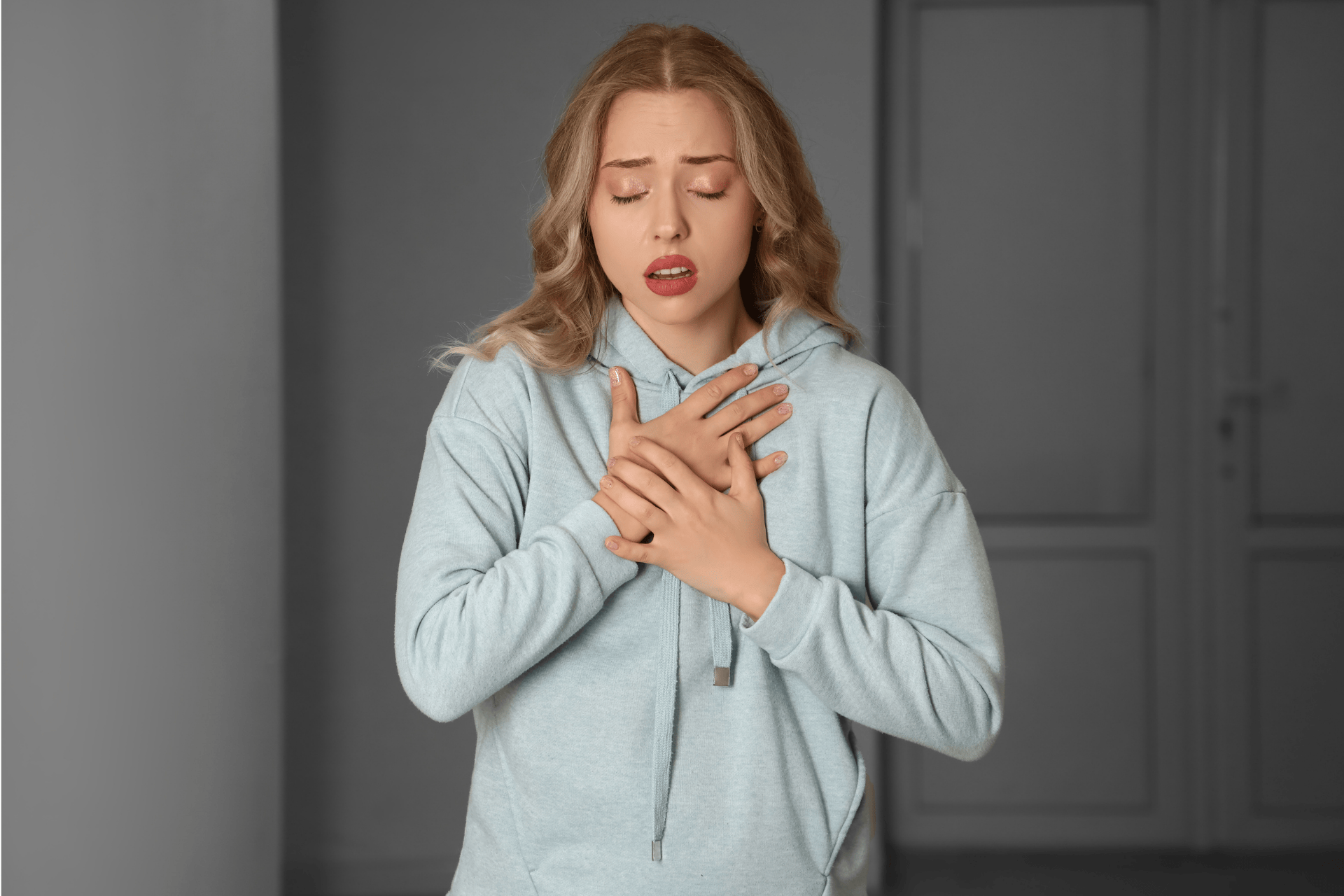Woman in a light hoodie, clutching her chest and appearing to have difficulty breathing.Woman in a light hoodie, clutching her chest and appearing to have difficulty breathing.