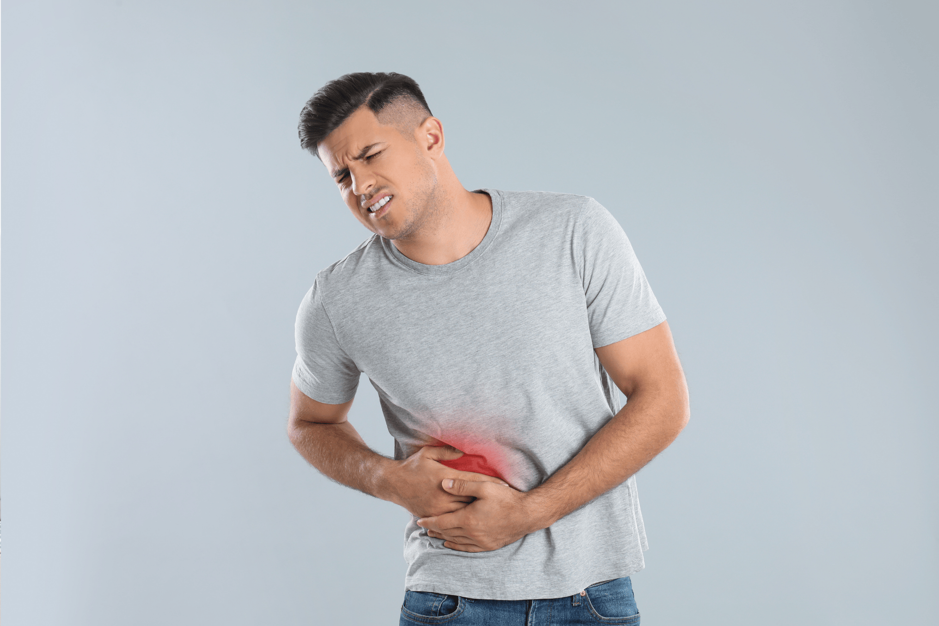 Man in a gray shirt clutching his abdomen in pain.