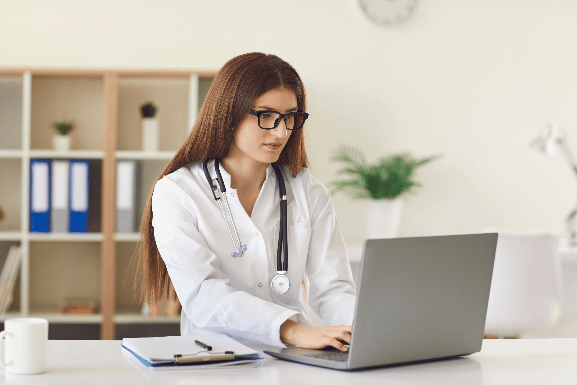 Female doctor with a stethoscope working on a laptop at her desk.